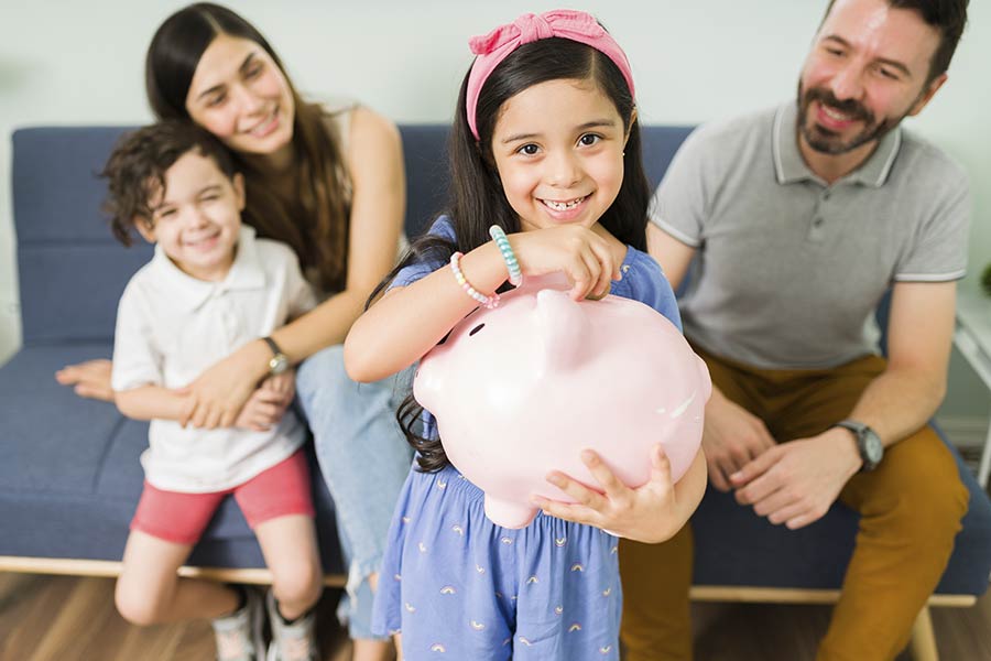 una bambina con la sua famiglia mentre mette un soldino in un salvadanaio